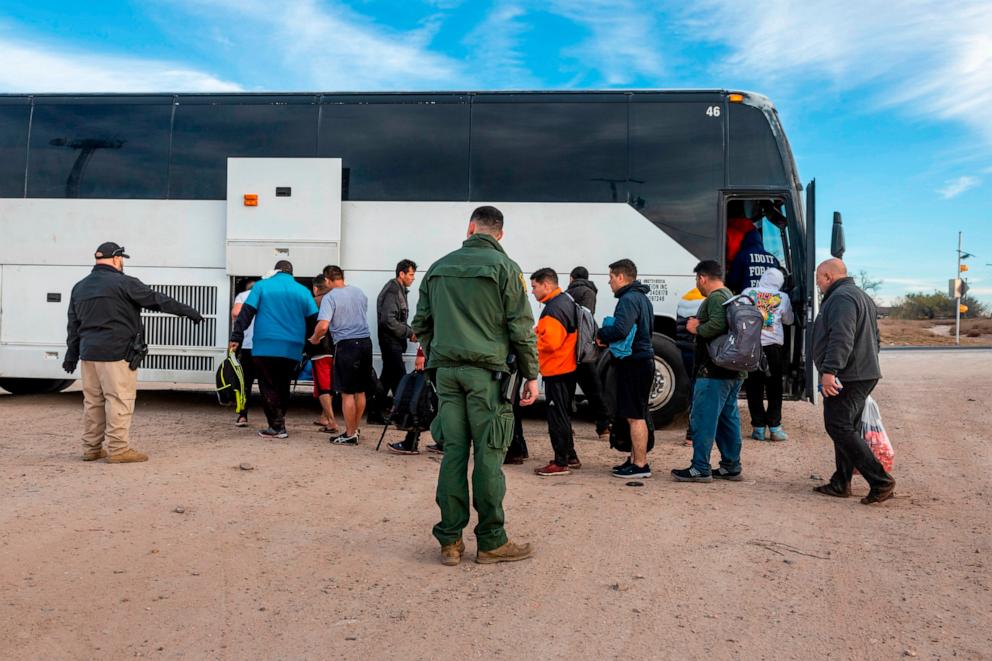 Immigrants file into a U.S. Customs and Border Protection bus after crossing the U.S.
